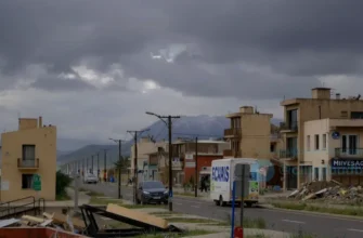 A photorealistic scene of a Chilean coastal city during a magnitude 6.7 earthquake, showing cracked streets, tilted buildings, dust and debris clouds, and the distant Andes mountains under a dramatic sky