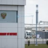 A modern Russian Ministry of Defense building with patriotic symbols like the Russian flag and military insignia, showing industrial facilities in the background with subtle camouflage netting and security personnel, no text or letters visible