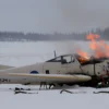 A small Antonov An-2 or similar biplane crashing on a snowy field in the Russian Sakhalin region, flames and smoke rising from the wreckage, snow-covered terrain, distant pine trees, overcast winter sky, realistic details, no text or logos